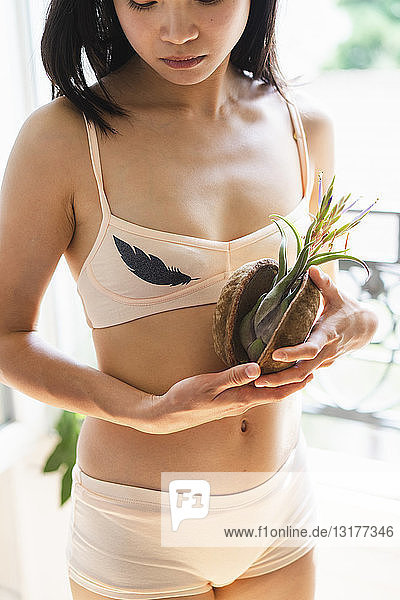 Attraktive junge Frau in Dessous steht am Fenster und hält eine Pflanze