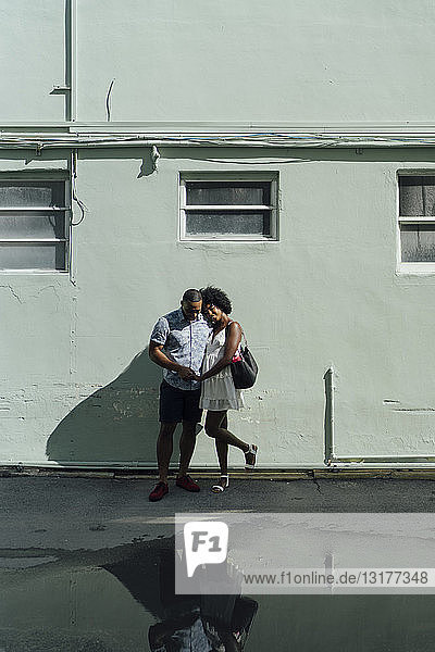 Lächelndes junges Paar steht am Gebäude an einer Pfütze