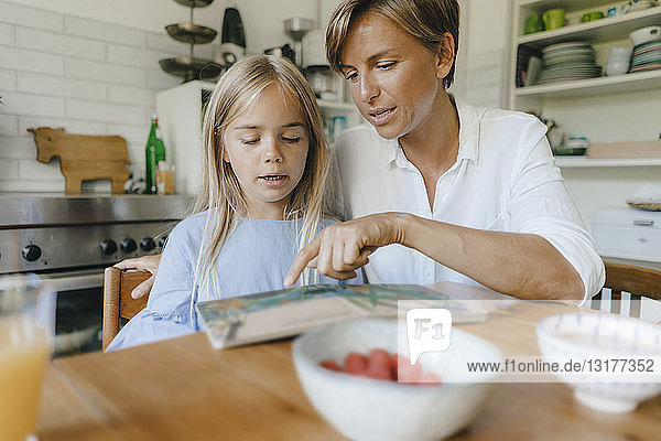 Mother and daughter reading book at table at home together