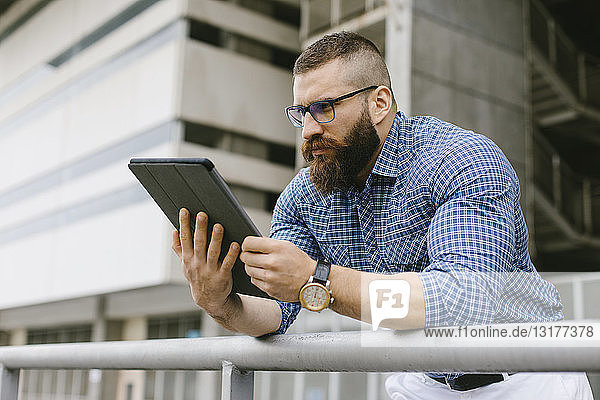Bearded hipster businessman wearing glasses  wrist watch and plaid shirt using digital tablet