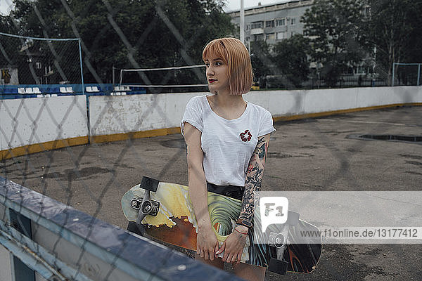 Coole junge Frau hält Carver-Skateboard im Freien
