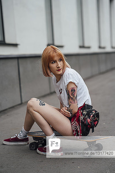 Young woman sitting on carver skateboard on the sidewalk
