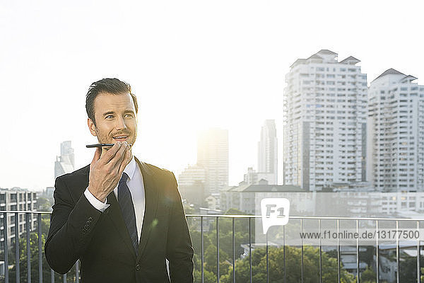 Business man in dark suit speaking into smartphone on city rooftop