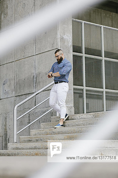 Bearded hipster businessman checking the time while walking downstairs