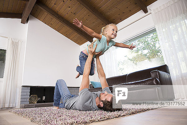 Vater spielt zu Hause mit Tochter auf Teppich im Wohnzimmer