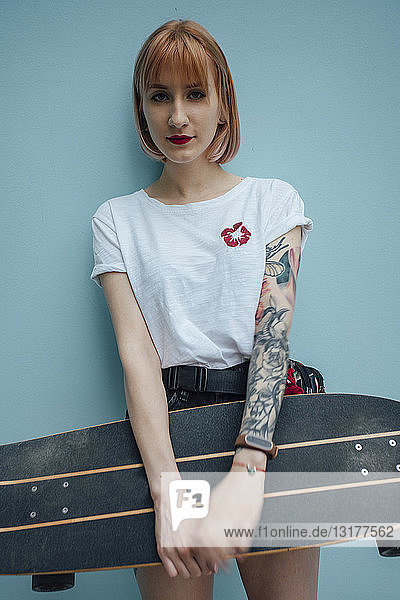 Porträt einer kühlen jungen Frau  die ein Carver-Skateboard hält und an einer türkisfarbenen Wand steht