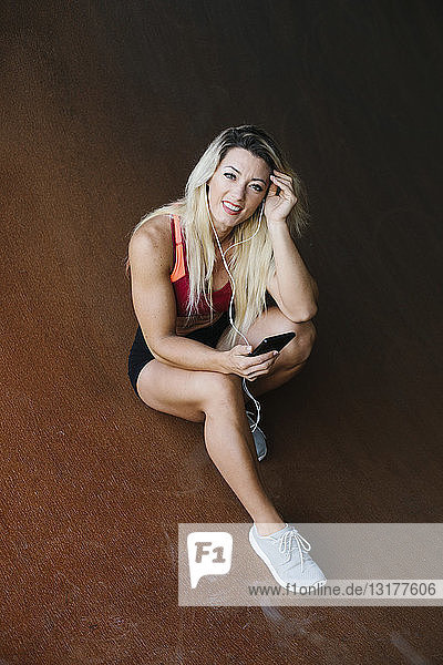 Porträt einer lächelnden athletischen Frau mit Mobiltelefon und Kopfhörern