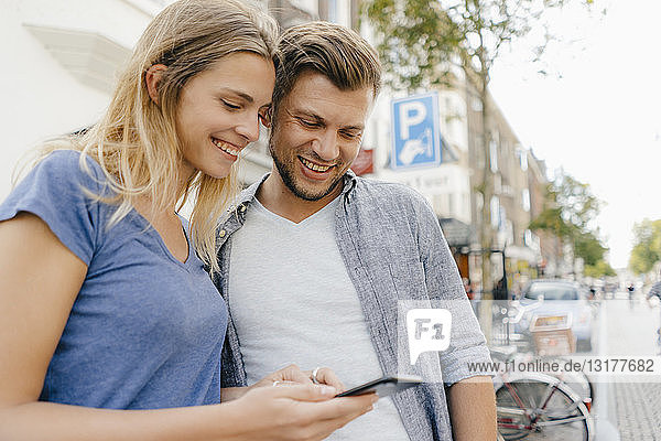 Niederlande  Maastricht  glückliches junges Paar beim Blick auf das Handy in der Stadt