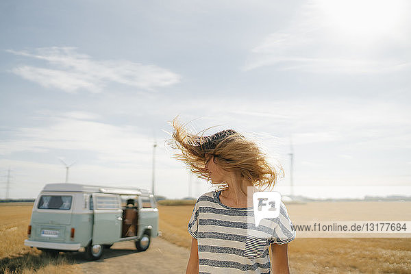 Blonde junge Frau im Wohnmobil in ländlicher Landschaft schüttelt ihr Haar
