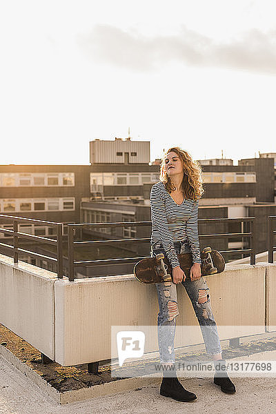 Young woman with skateboard enjoying sunset on roof terrace