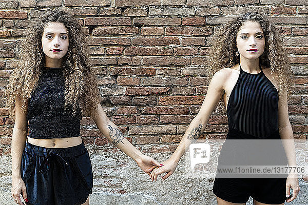 Porträt von Zwillingsschwestern in Schwarz gekleidet  die Hände halten