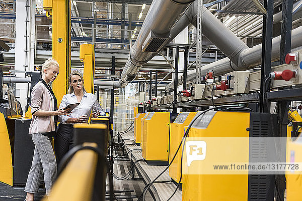 Two women with tablet looking at machine in factory shop floor