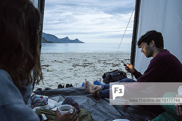 Norway  Lapland  Young people camping in a tent on a beach at fjord