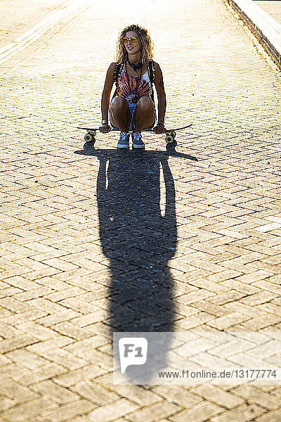 Junge Frau sitzt auf einem Skateboard im Sonnenlicht