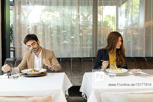 Man eating and woman using tablet in a restaurant
