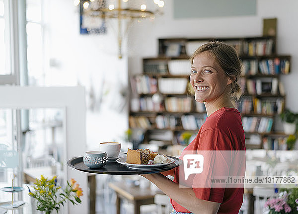 Portrait of smiling young woman serving coffee and cake in a cafe