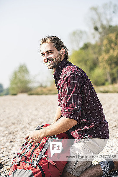 Lächelnder junger Mann mit Rucksack am Kieselsteinufer