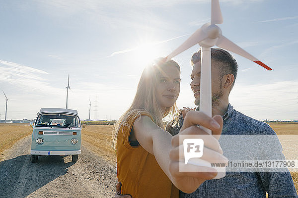 Junges Paar im Wohnmobil in ländlicher Landschaft mit Modell einer Windkraftanlage