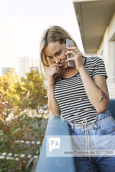 Lächelnde junge Frau telefoniert per Handy auf dem Balkon