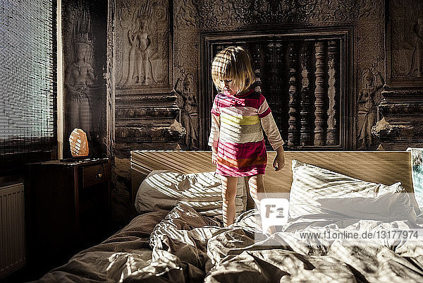 Little girl standing on parent's bed at home