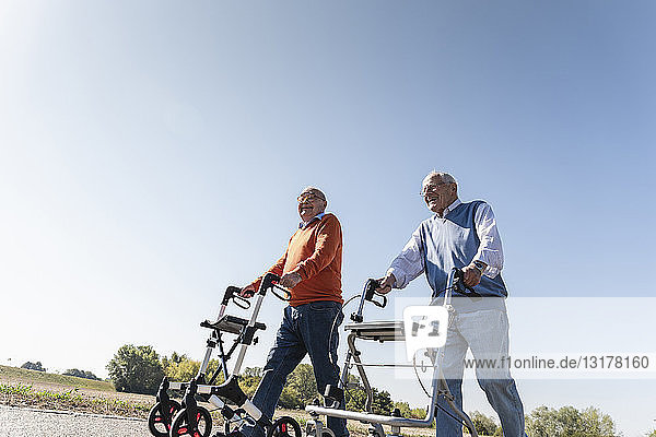 Zwei alte Freunde gehen auf einer Landstraße und benutzen Rollatoren