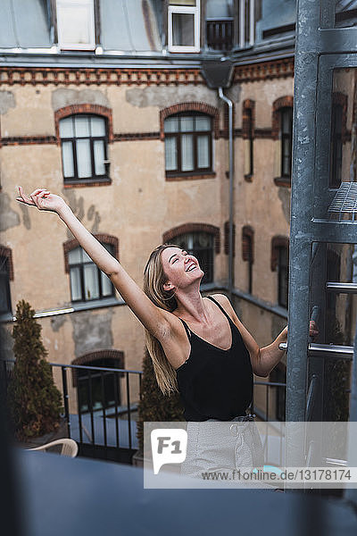 Glückliche junge Frau klettert auf dem Balkon auf eine Feuertreppe