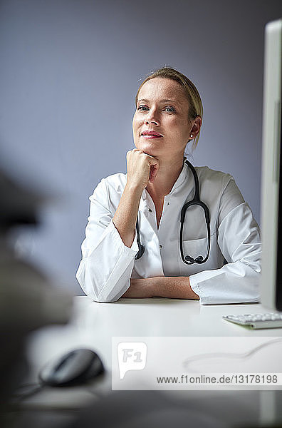 Porträt einer Ärztin mit Stethoskop am Schreibtisch sitzend