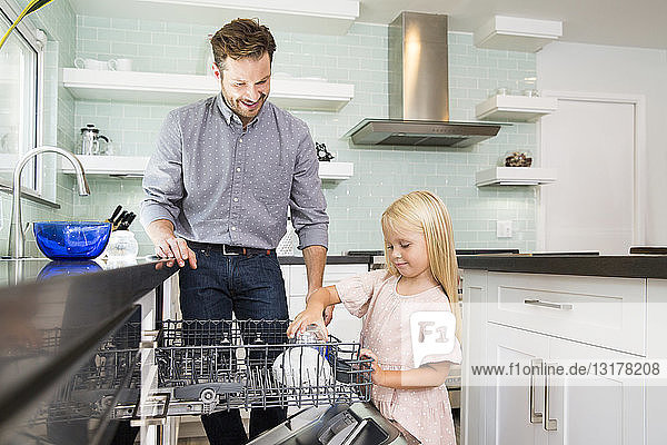 Mädchen hilft Vater beim Abräumen des Geschirrspülers in der Küche