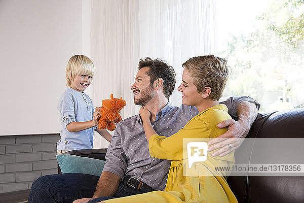 Eltern umarmen sich zu Hause auf der Couch und Junge spielt mit Kuscheltier