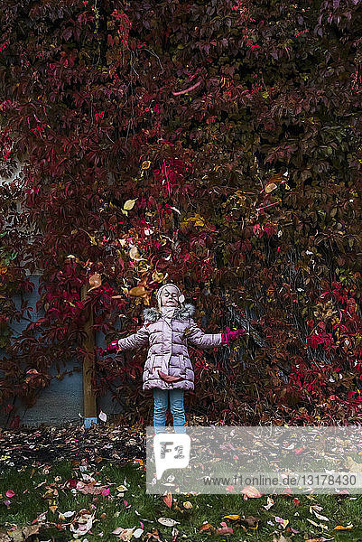 Mädchen wirft im Garten Herbstblätter in die Luft