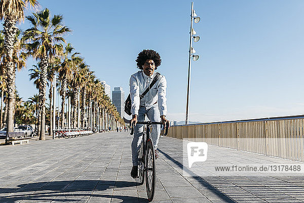 Mittelgroßer erwachsener Mann  der auf einer Strandpromenade Fahrrad fährt und Musik hört