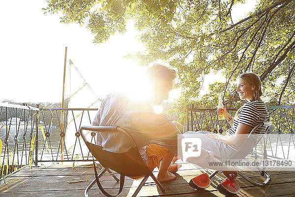 Young couple sitting on a jetty at a lake eating watermelon