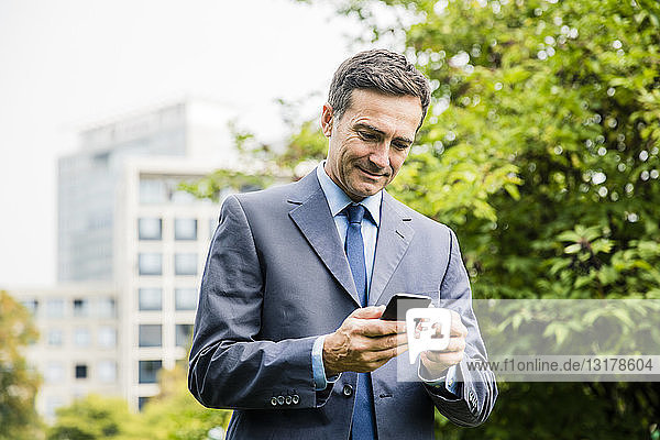 Businessman using cell phone in city park