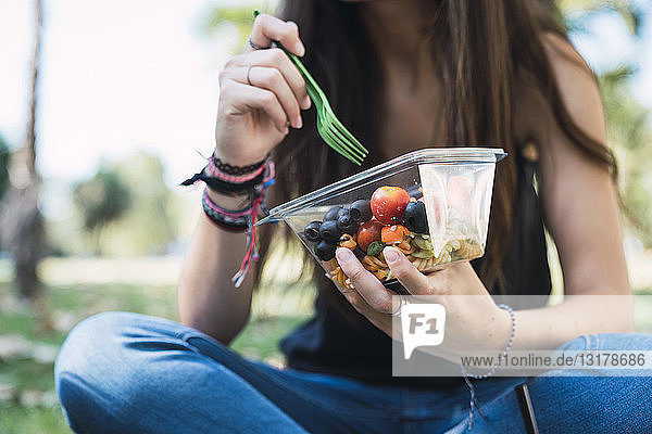 Junge Frau sitzt in einem Park und isst Salat