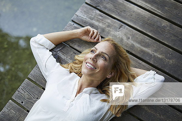 Lächelnde blonde Frau liegt auf einem Holzsteg an einem See