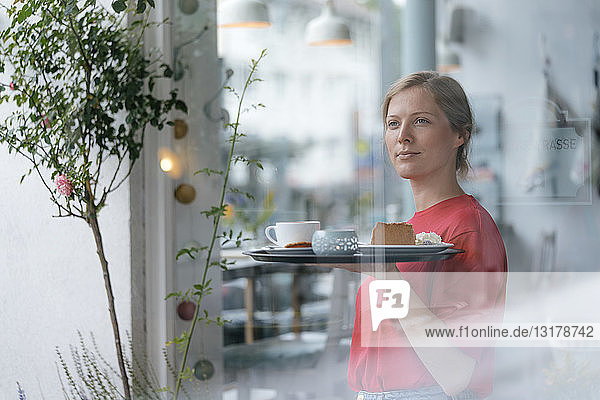 Junge Frau serviert Kaffee und Kuchen in einem Café