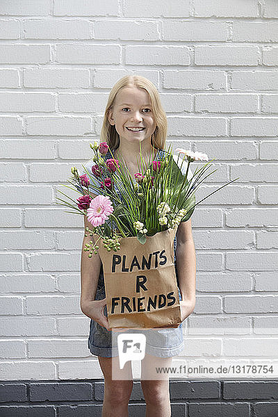 Porträt eines lächelnden Mädchens mit Papiertüte mit Blumen