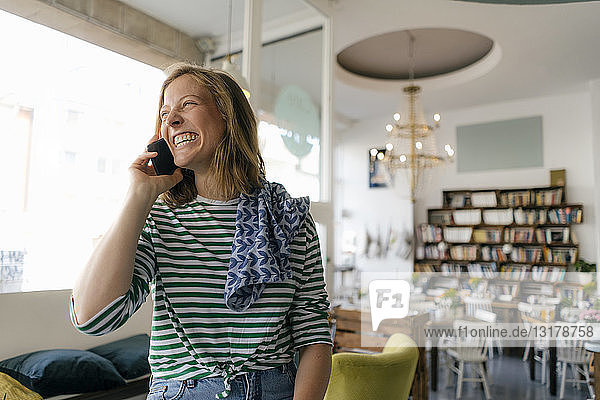 Lachende junge Frau am Handy in einem Cafe