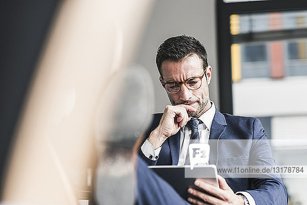 Geschäftsmann  der ein digitales Tablett verwendet und mit erhobenen Füßen im Büro sitzt