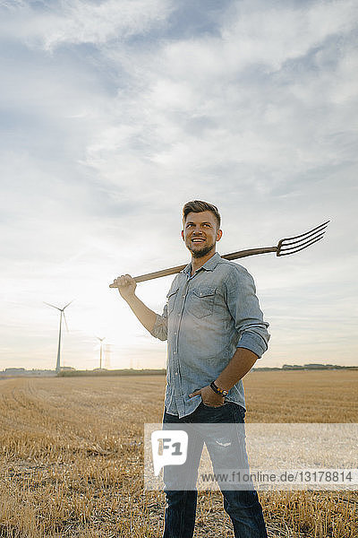 Portrait of smiling young man holding pitchfork standing on stubble field