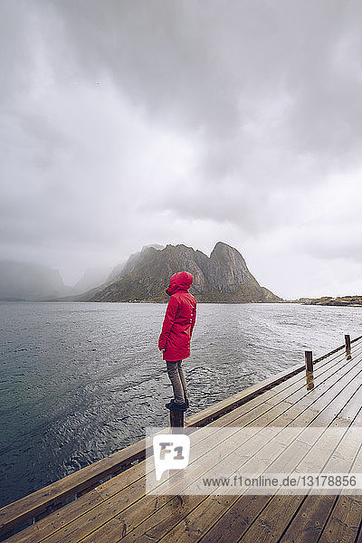 Norwegen  Lofoten  Hamnoy  Mann in roter Regenjacke auf Holzpfahl stehend  schaut in die Ferne