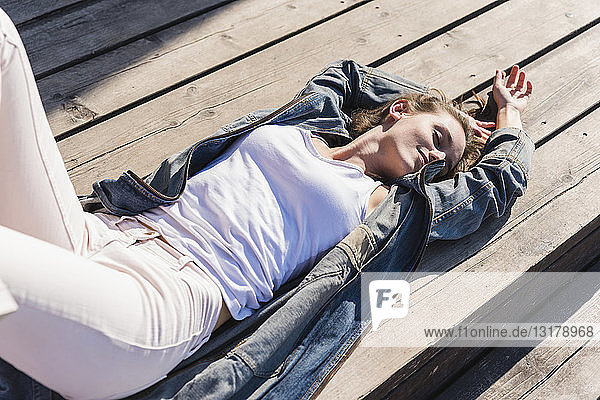 Entspannte junge Frau liegt auf Holzbrettern im Sonnenschein