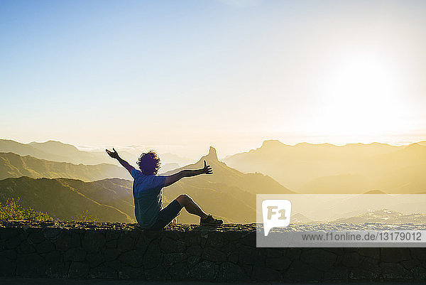 Spain  Canary Islands  Gran Canaria  back view of happy man watching mountain landscape at sunset