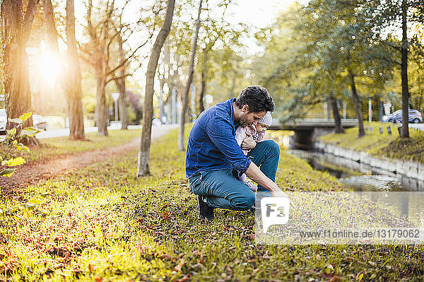 Father searching for chestnuts in park  with baby daughter on his lap