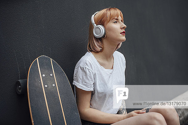 Junge Frau mit Skateboard und Kopfhörern beim Musikhören