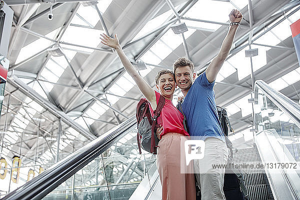 Glückliches Paar jubelt auf der Rolltreppe am Flughafen