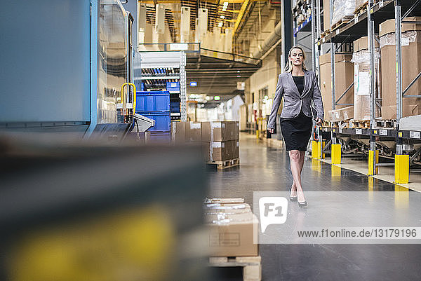 Woman with tablet walking in factory storehouse