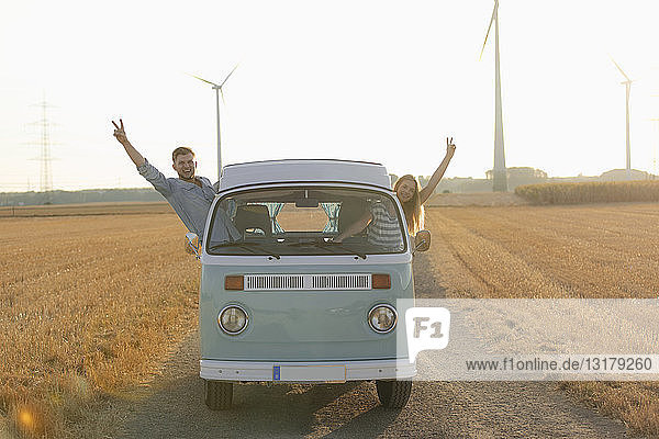 Happy couple leaning out of window of a camper van in rural landscape