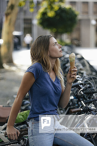 Niederlande  Maastricht  blonde junge Frau hält Eiswaffel in der Stadt am Fahrradständer