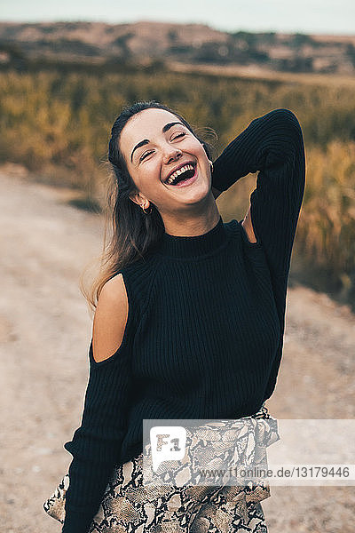 Porträt einer lachenden jungen Frau in der Natur  die einen modischen schwarzen Pullover trägt